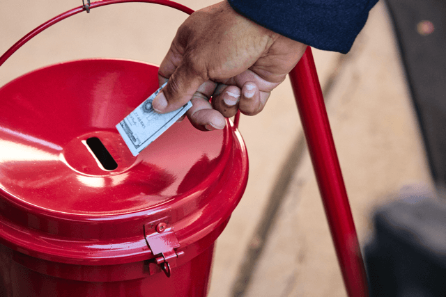 A happy child ringing a bell in front of a Salvation Army kettle.
