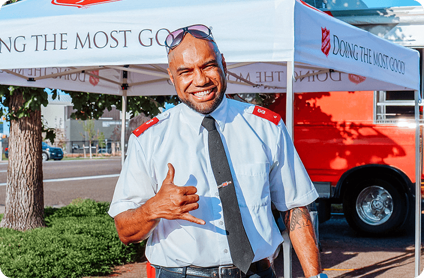 Smiling Salvation Army officer standing outside near a Red Kettle tent.